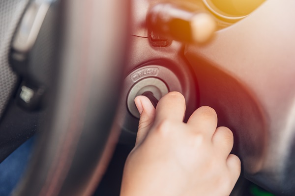 Close-up of a young person’s hand turning a car key in the ignition, with part of the steering wheel and dashboard visible.