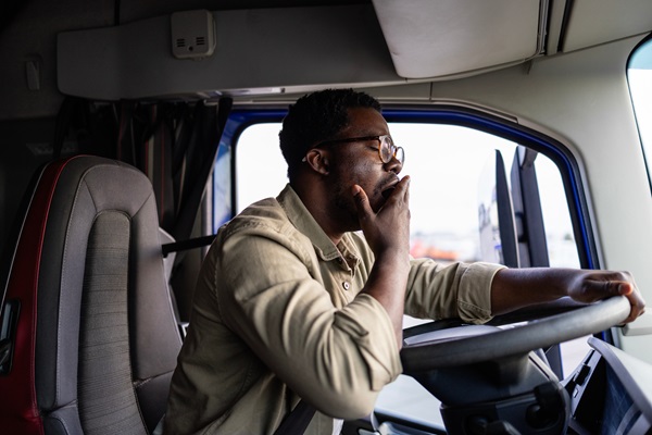 Truck driver feeling exhausted, yawning while driving.