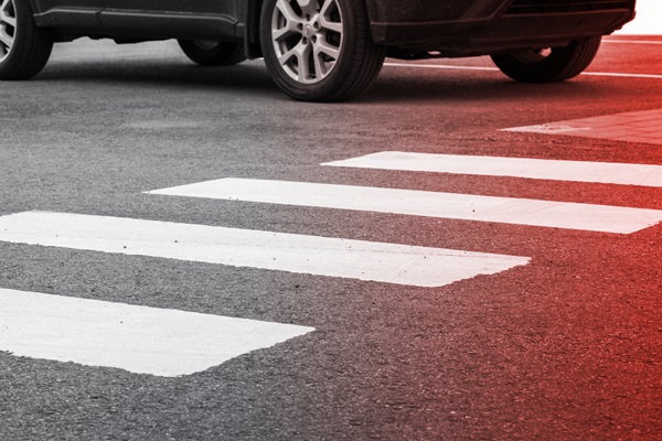 The front of a black SUV stops just short of a painted white crosswalk on dark asphalt, with a strong red light effect visible over the right side of the road.