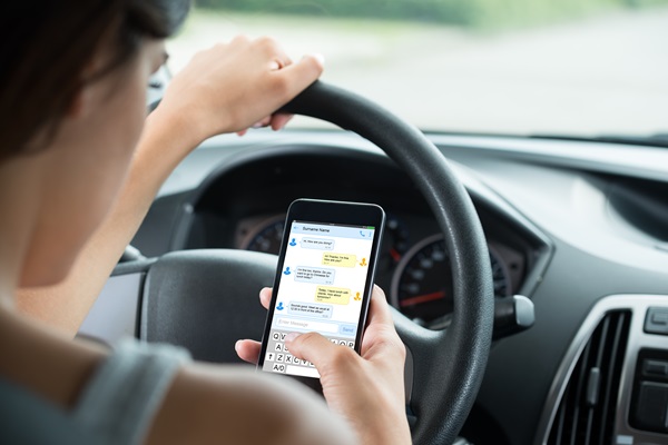 A driver typing a text message on a handheld smartphone while resting an arm on the steering wheel, a violation of Tennessee’s Hands-Free law and a major factor in distracted driving accident claims.