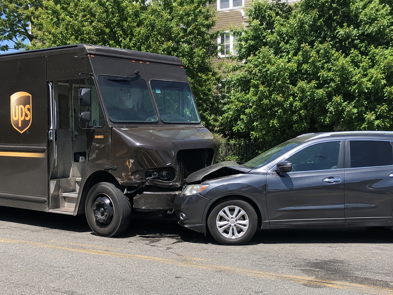 A UPS delivery truck and a gray SUV sit locked together on a Tennessee street after a front-end collision, with visible bumper and grille damage on both vehicles, depicting a commercial delivery vehicle accident that raises questions about UPS or FedEx corporate liability, driver negligence, and available insurance coverage under Tennessee law.